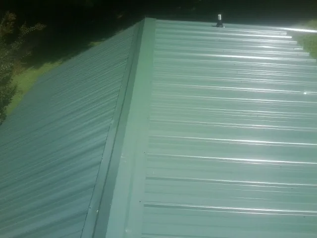 New green metal panels meeting at the ridge of a roof — Flat Roof Repair work by our crew in Pineville