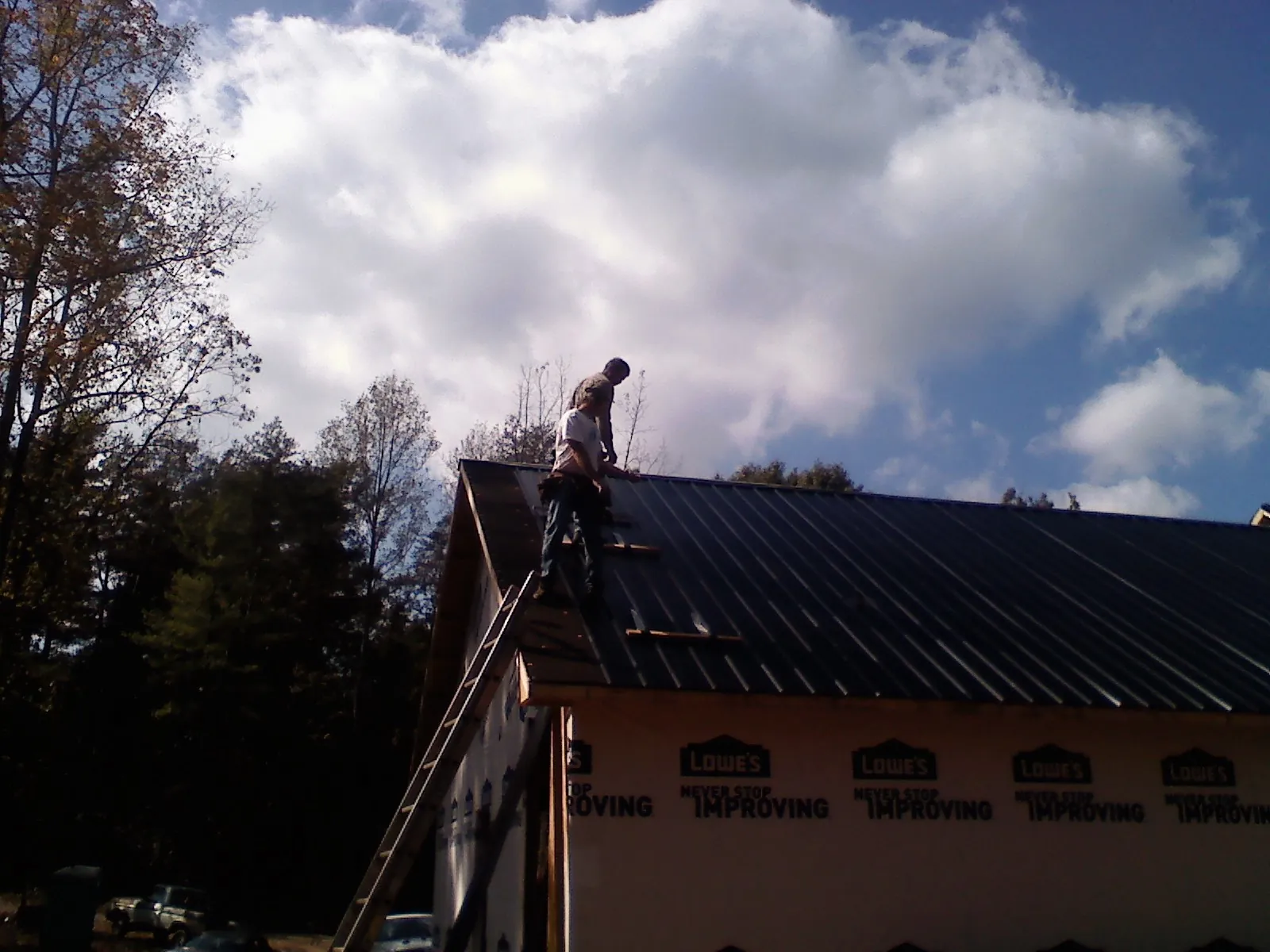 Roofer fastening dark metal panels high against a cloudy sky, from a Roof Inspection job in Pineville
