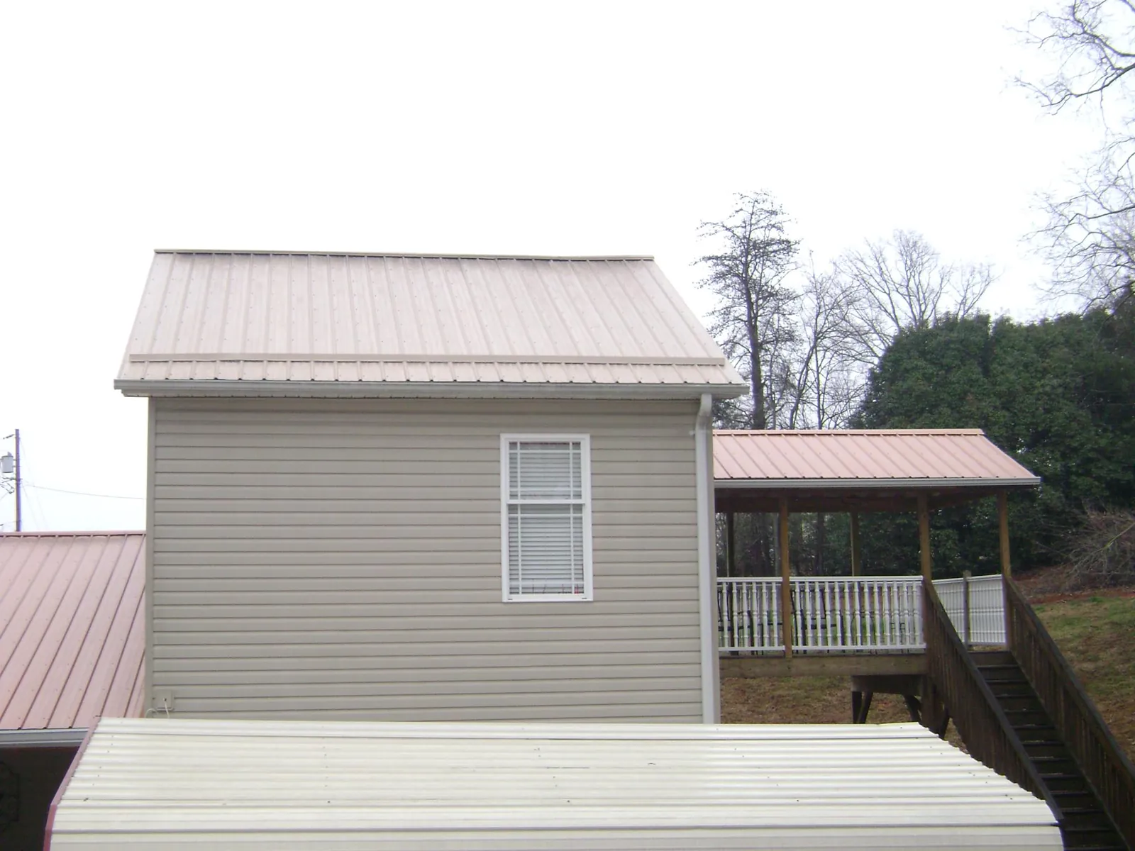 Tan metal roofs on a two story addition and attached porch, from a Roof Replacement job in Pineville
